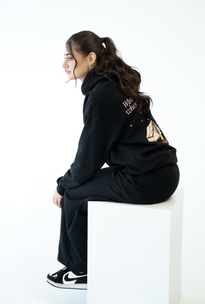 Person wearing a black tracksuit with visible branding on a white background